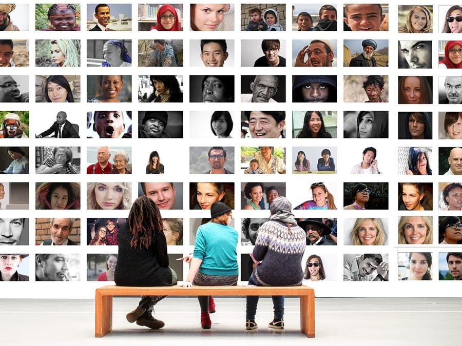 People sitting on a bench looking at a museum-style collage of diverse faces