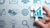 Image of a hand putting a puzle piece showing a map of growth in a puzzle with other iconography  related to career success, like an email and a lightbulb and a handshake and a magnifying glass.