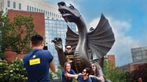 One student takes a picture of a group of students posing in front of the Mario the Magnificent statue.