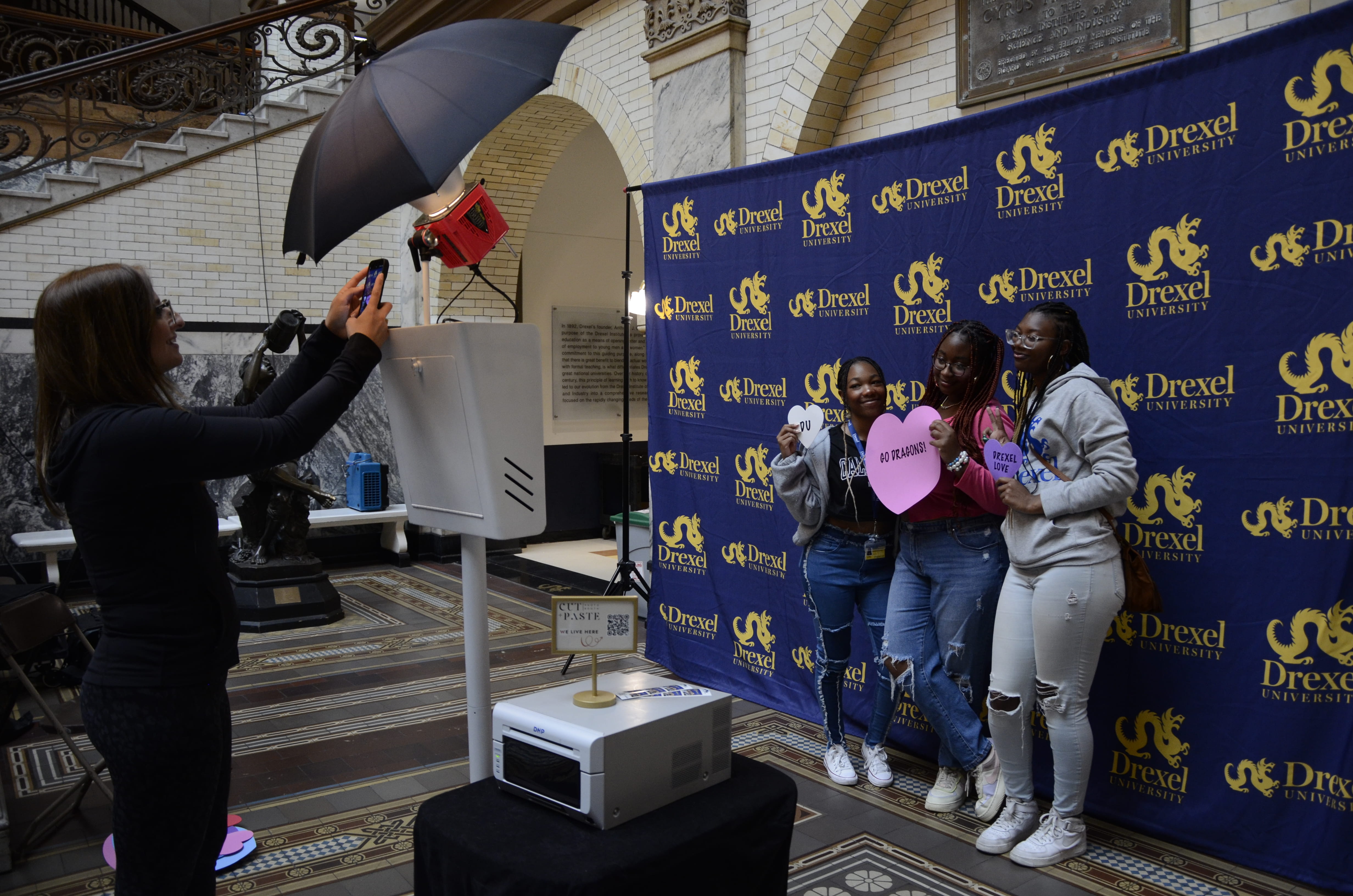 Three students pose for a photo in front of a Drexel background