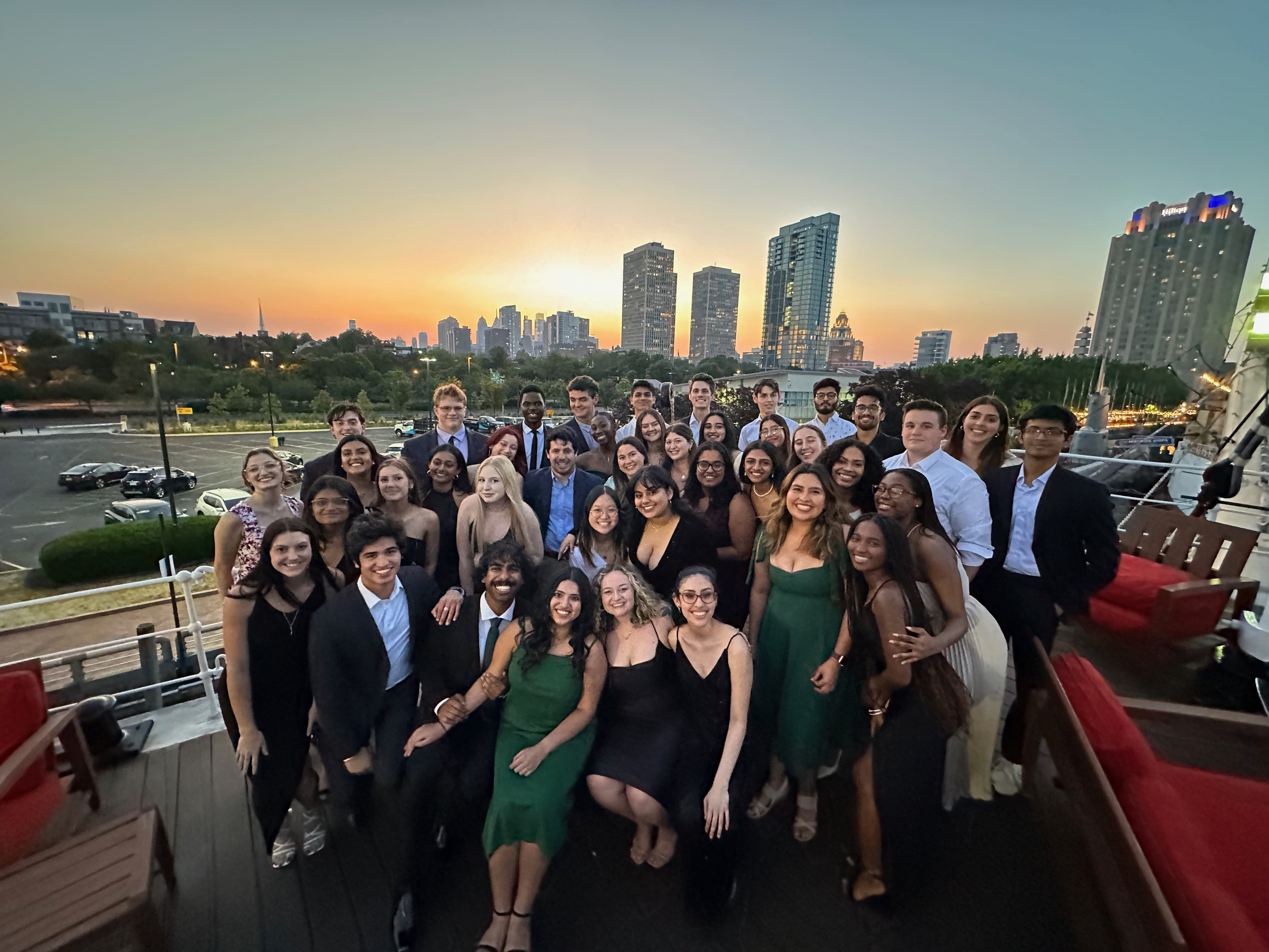 A group of students standing together with the Philadelphia skyline in the background at sunset.