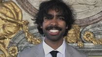 A photo of a man in a grey suit with black tie.