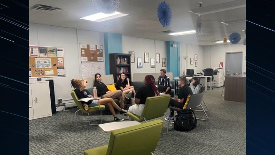 A group of students sitting on green couches and chairs in a room.
