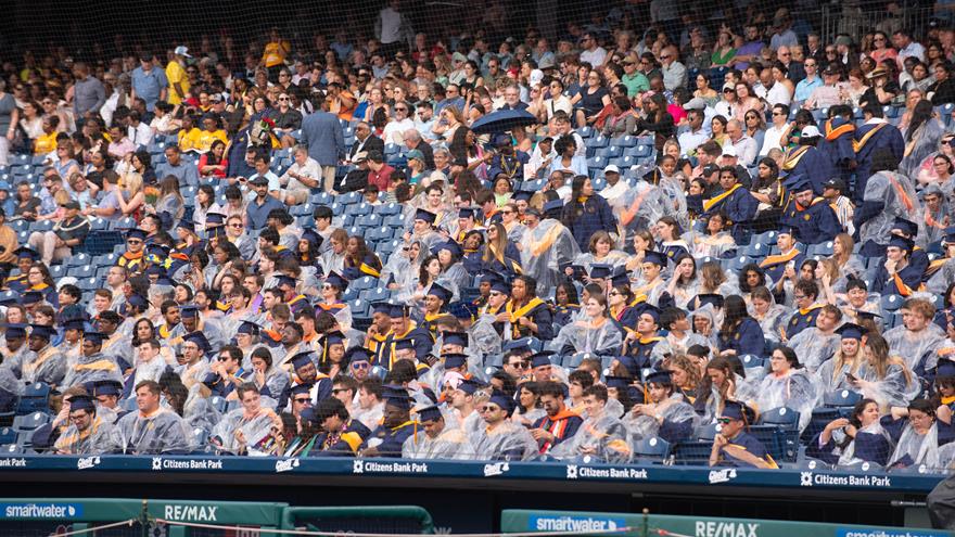 Students in Commencement regalia, some with ponchos and umbrellas, in the stands of Citizens Bank Park for Drexel&#39;s 2024 Commencement.