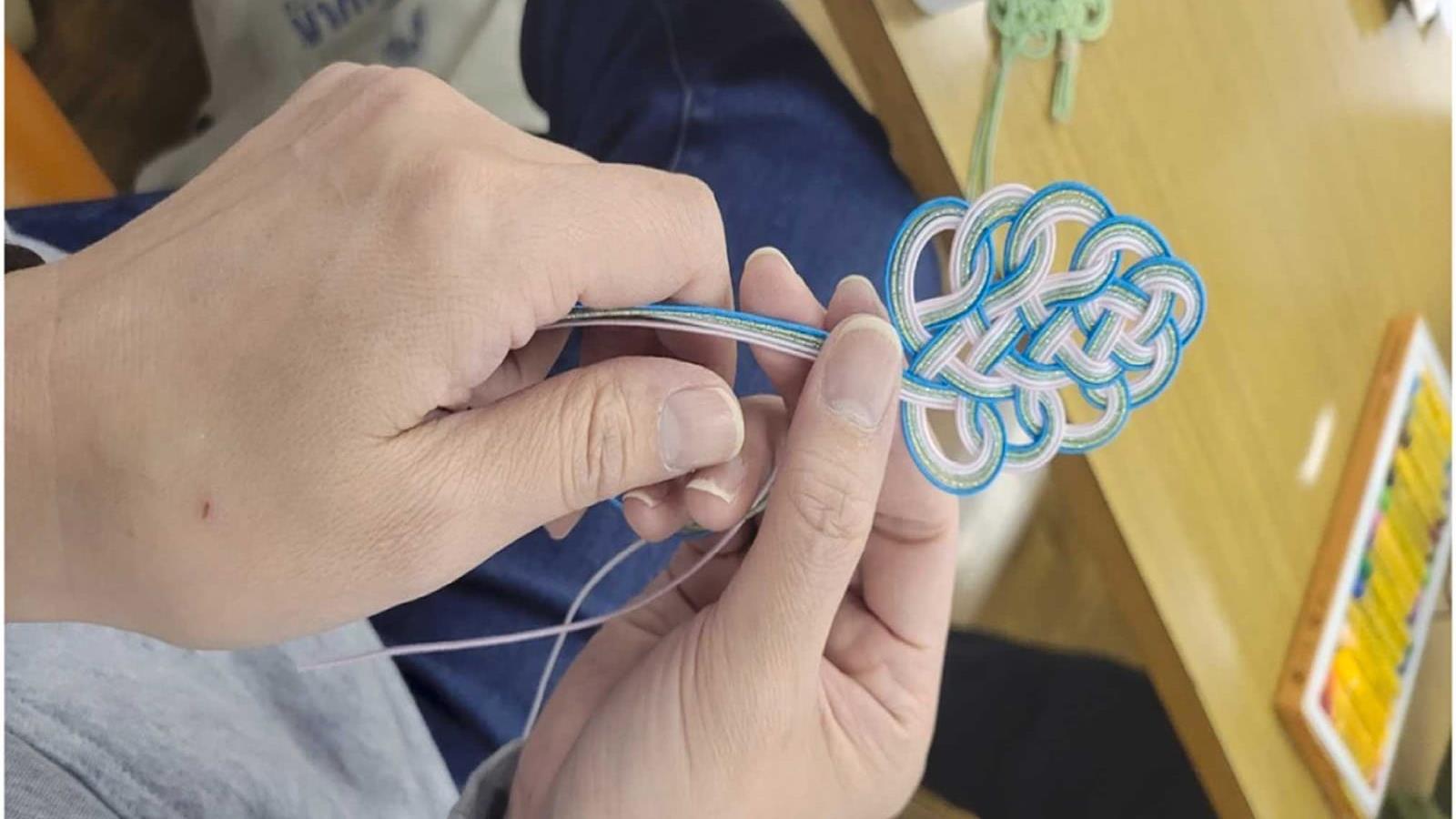 A pair of hands are weaving strings into a looped knot.