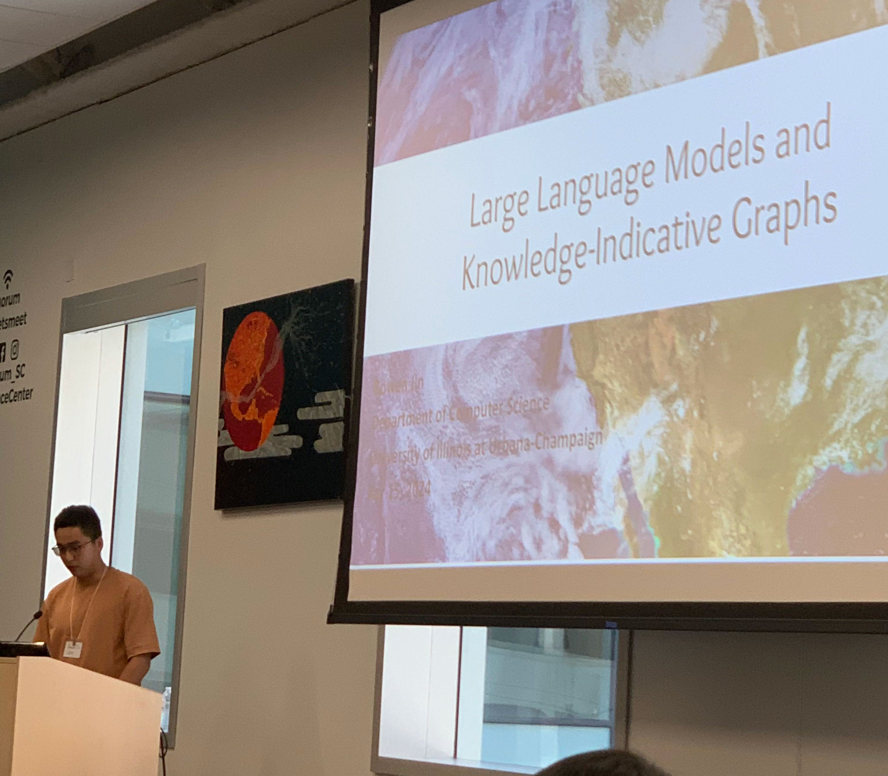 A presenter introduces a PowerPoint titled “Large Language Models and Knowledge-Indicative Graphs”